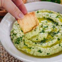 dipping pita chip into edamame hummus