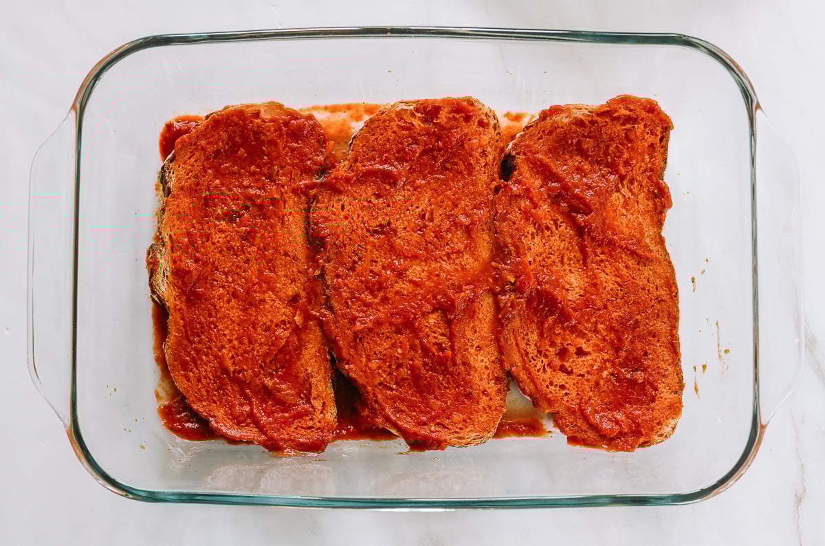 bread slices covered in marinara sauce in baking dish