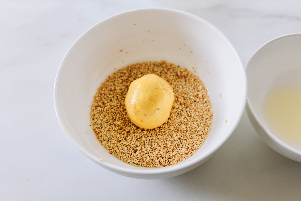 rolling wet dough in toasted sesame seeds