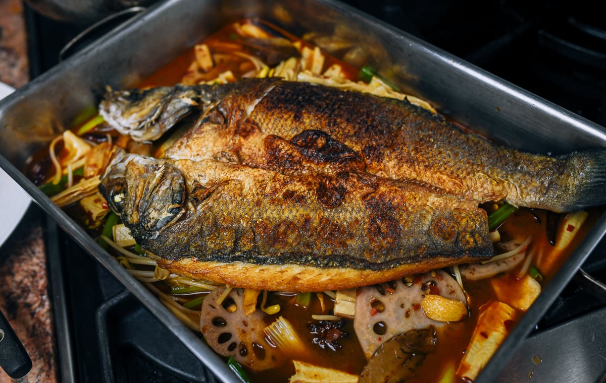 Roasted butterflied fish on top of spicy sauce and vegetable mixture in roasting pan