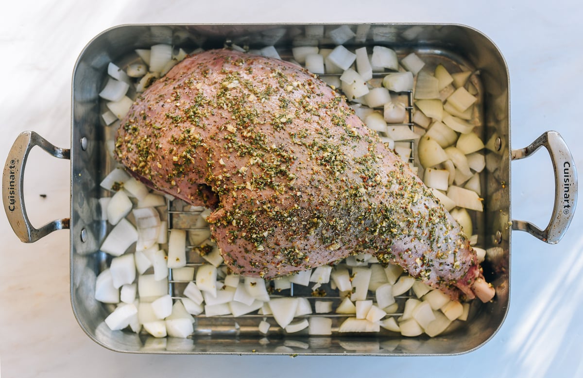 marinated leg of lamb on rack with onions in base of roasting pan