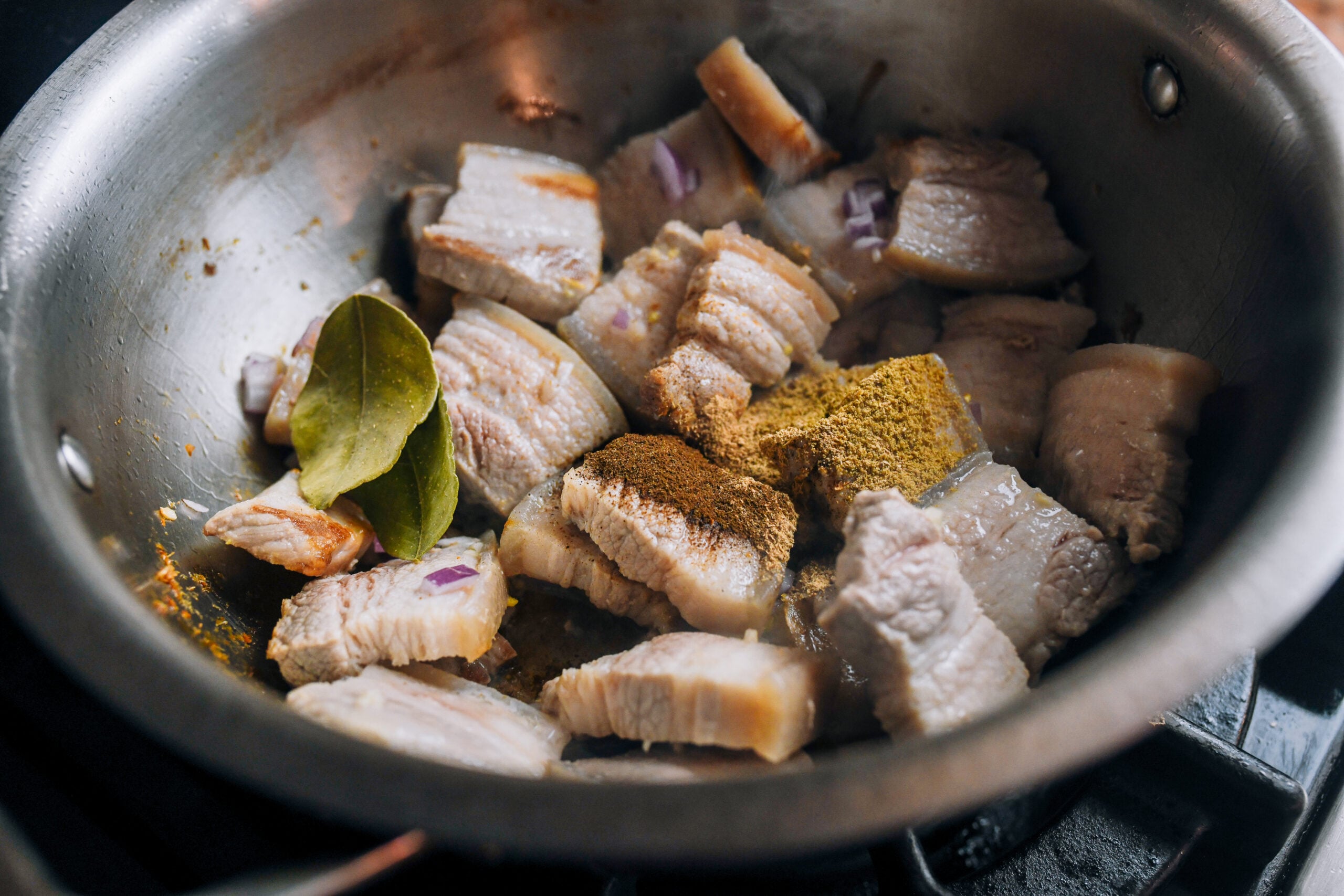 Adding spices and aromatics to pork belly in pot