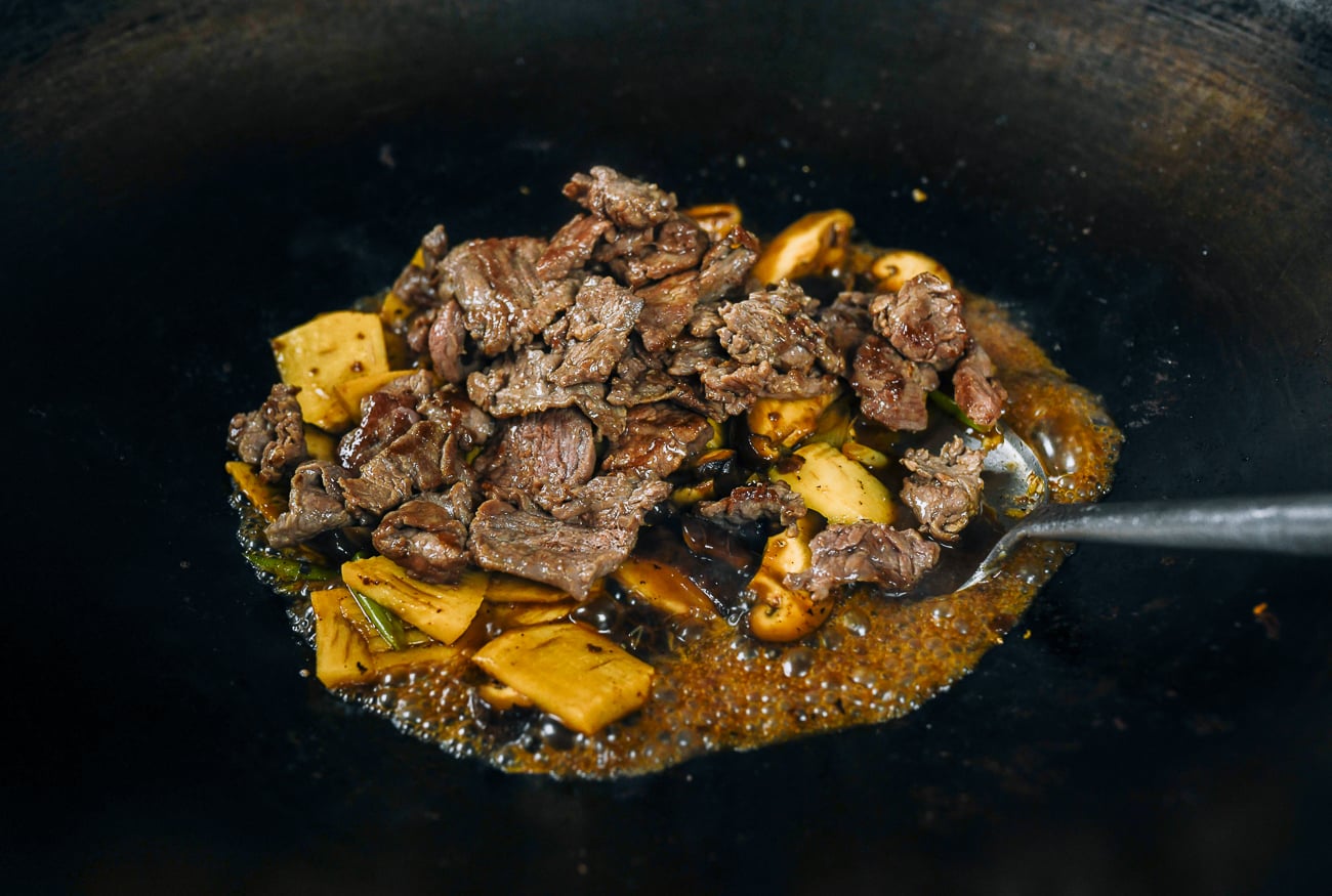 adding beef to bamboo shoots and mushrooms