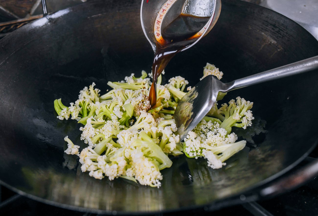 pouring sauce in to wok with cauliflower