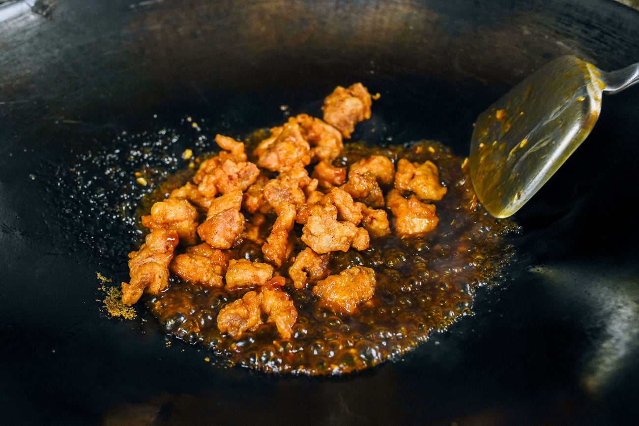 tossing fried chicken pieces into wok with sauce