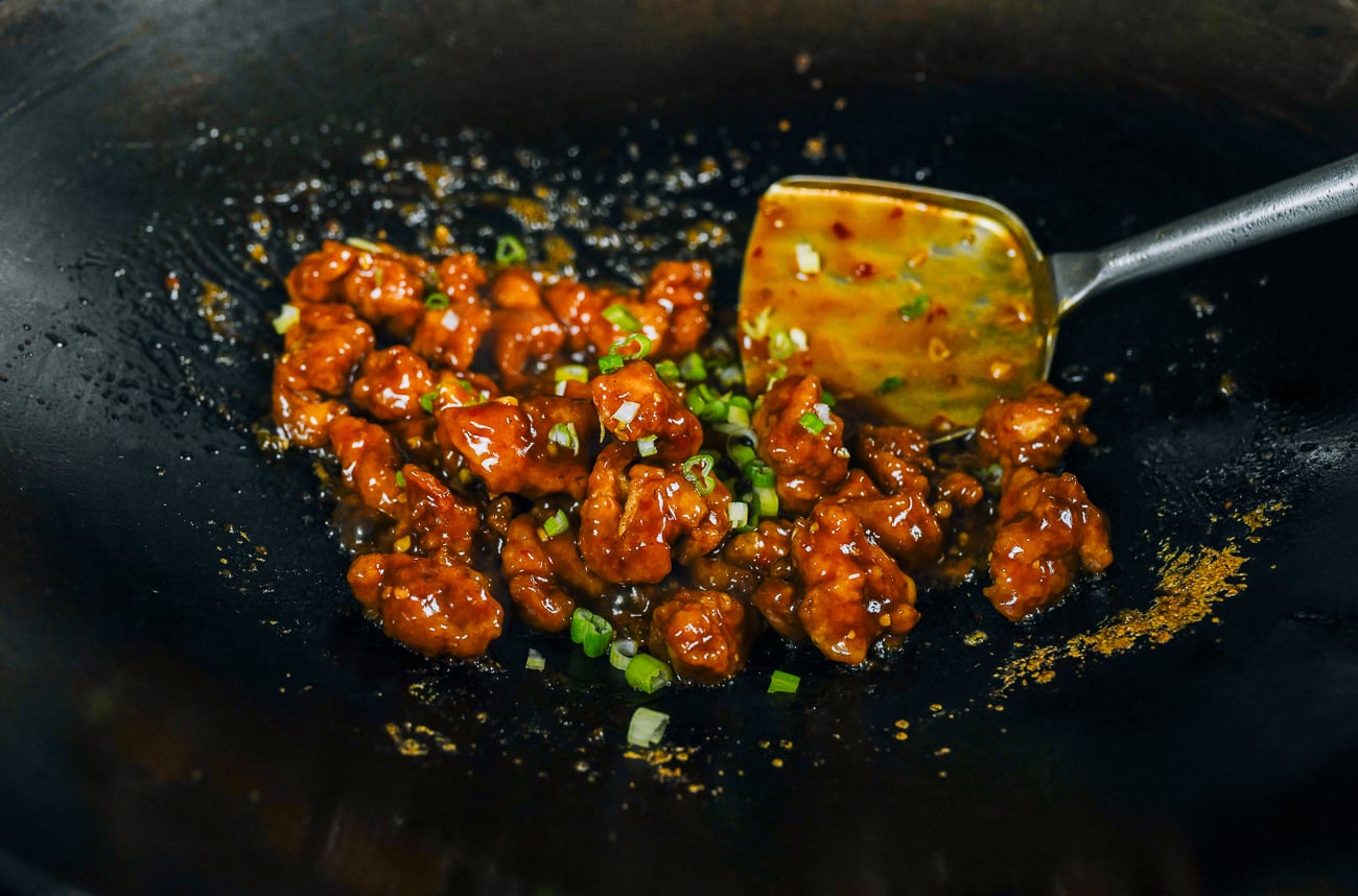 tossing chicken and spicy sauce together with scallions
