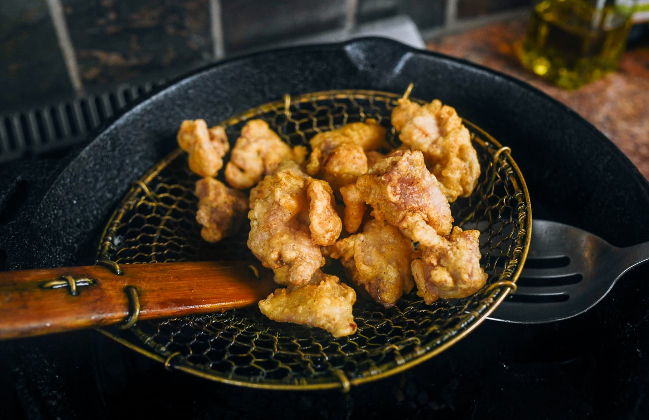 removing fried chicken pieces from oil with a chinese spider