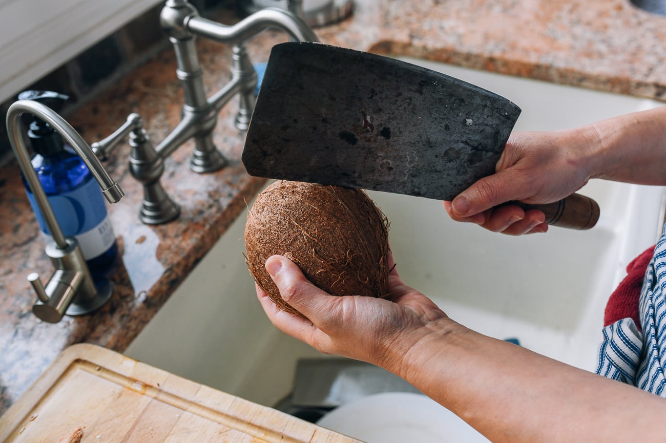 cracking open a mature coconut with the back of a cleaver
