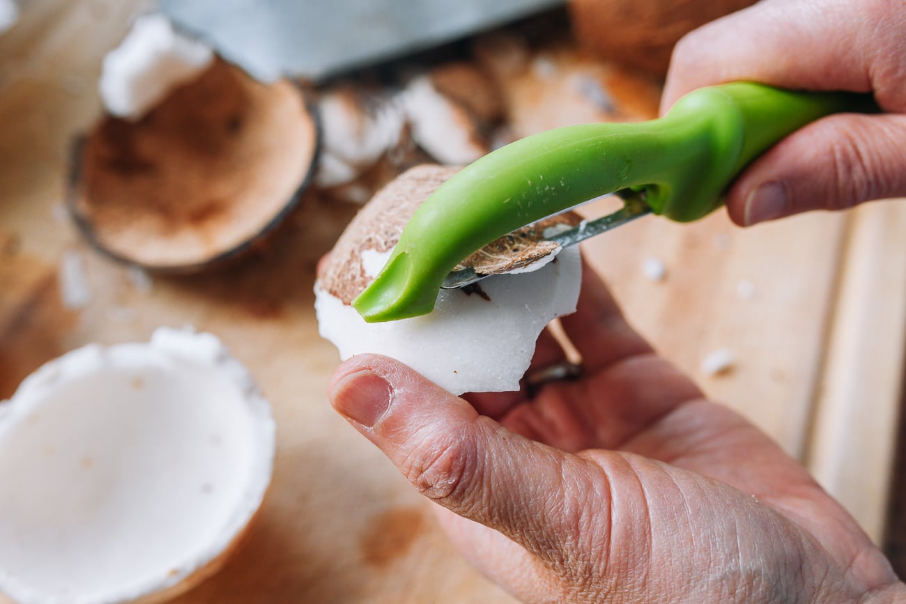 peeling brown skin off of coconut flesh with a peeler