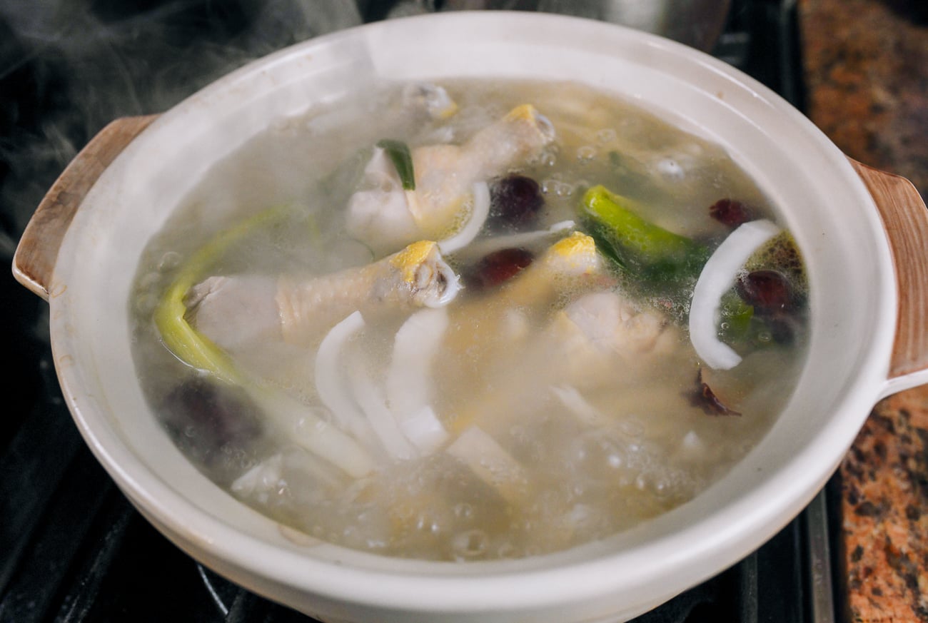 adding chicken legs to soup pot with coconut