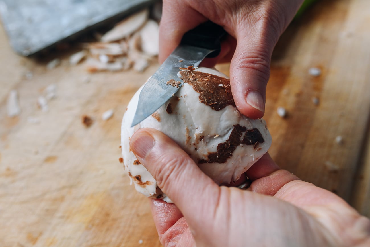 peeling brown skin off of coconut flesh with a paring knife