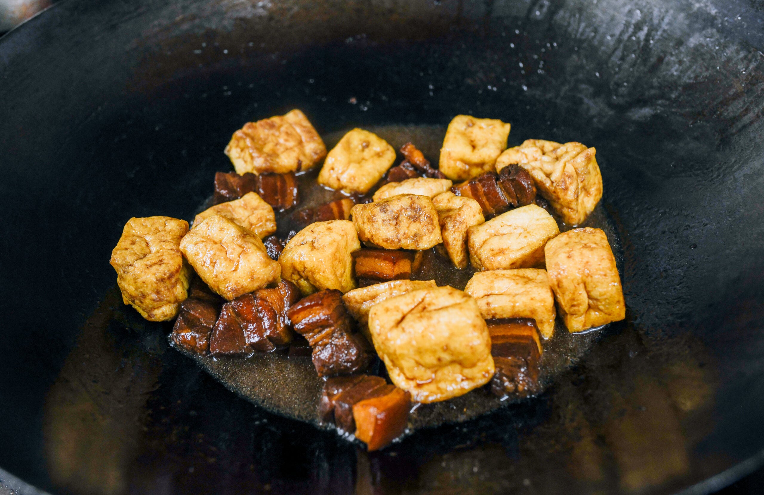 adding tofu puffs to pork belly in wok
