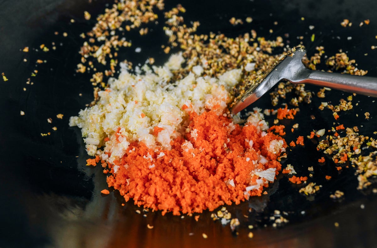 adding finely chopped napa cabbage and carrot to wok with mushrooms