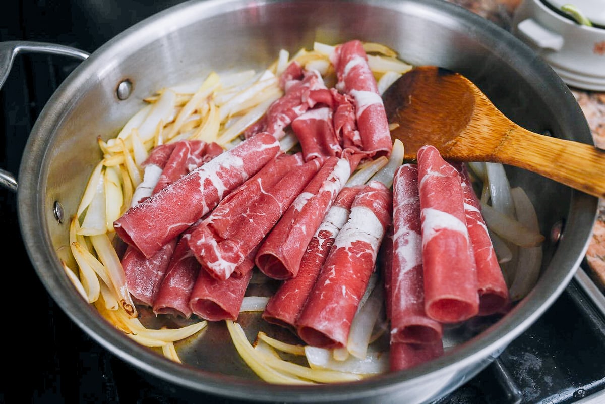 adding thinly shaved hot pot beef to onions
