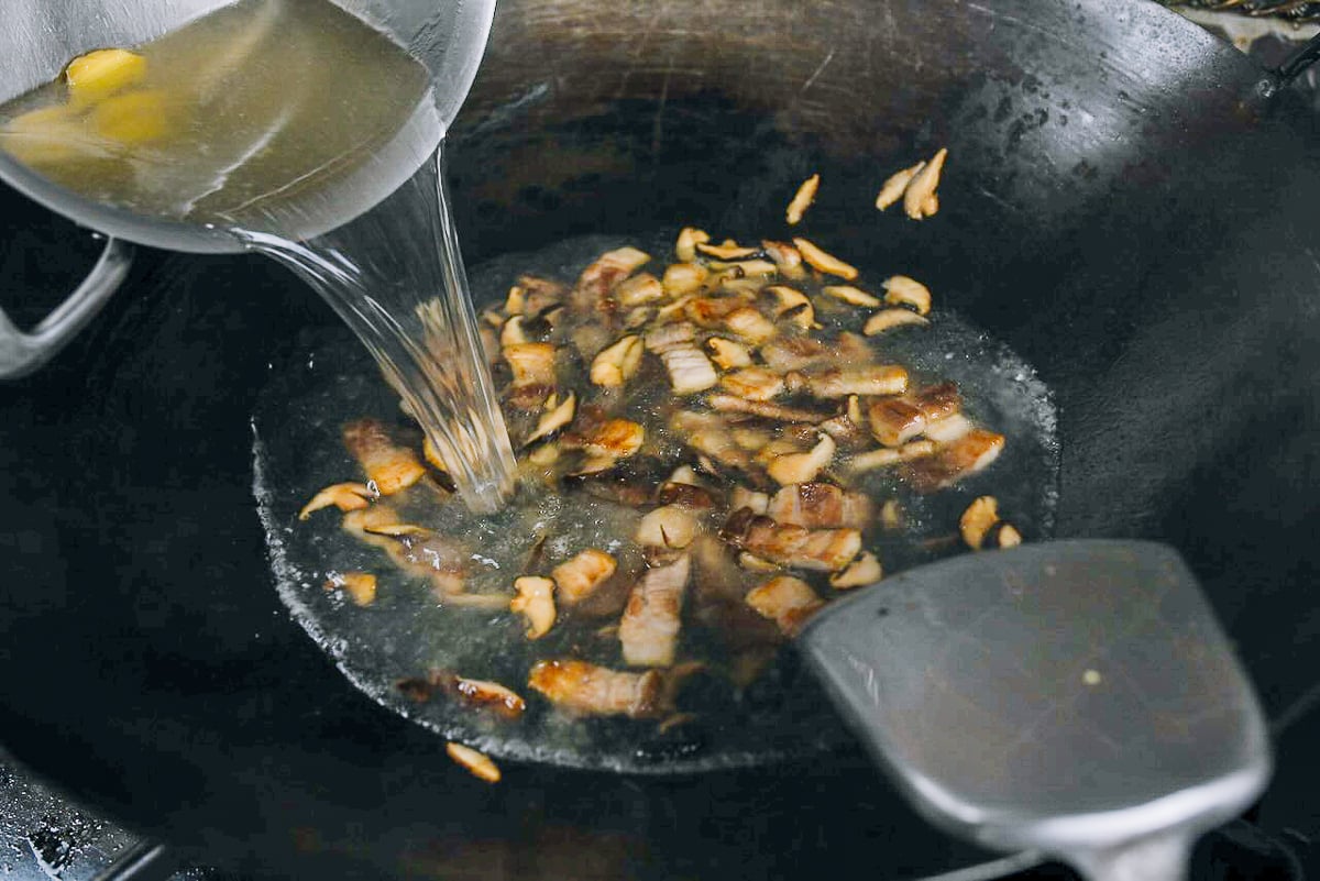 adding pork stock to pork belly and mushrooms in wok