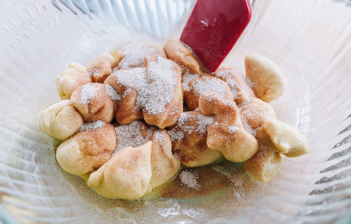 dough pieces coated in butter and cinnamon sugar in glass bowl