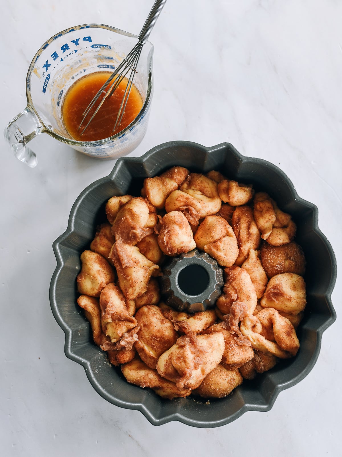 proofed monkey bread in bundt pan with sauce mixture in measuring cup